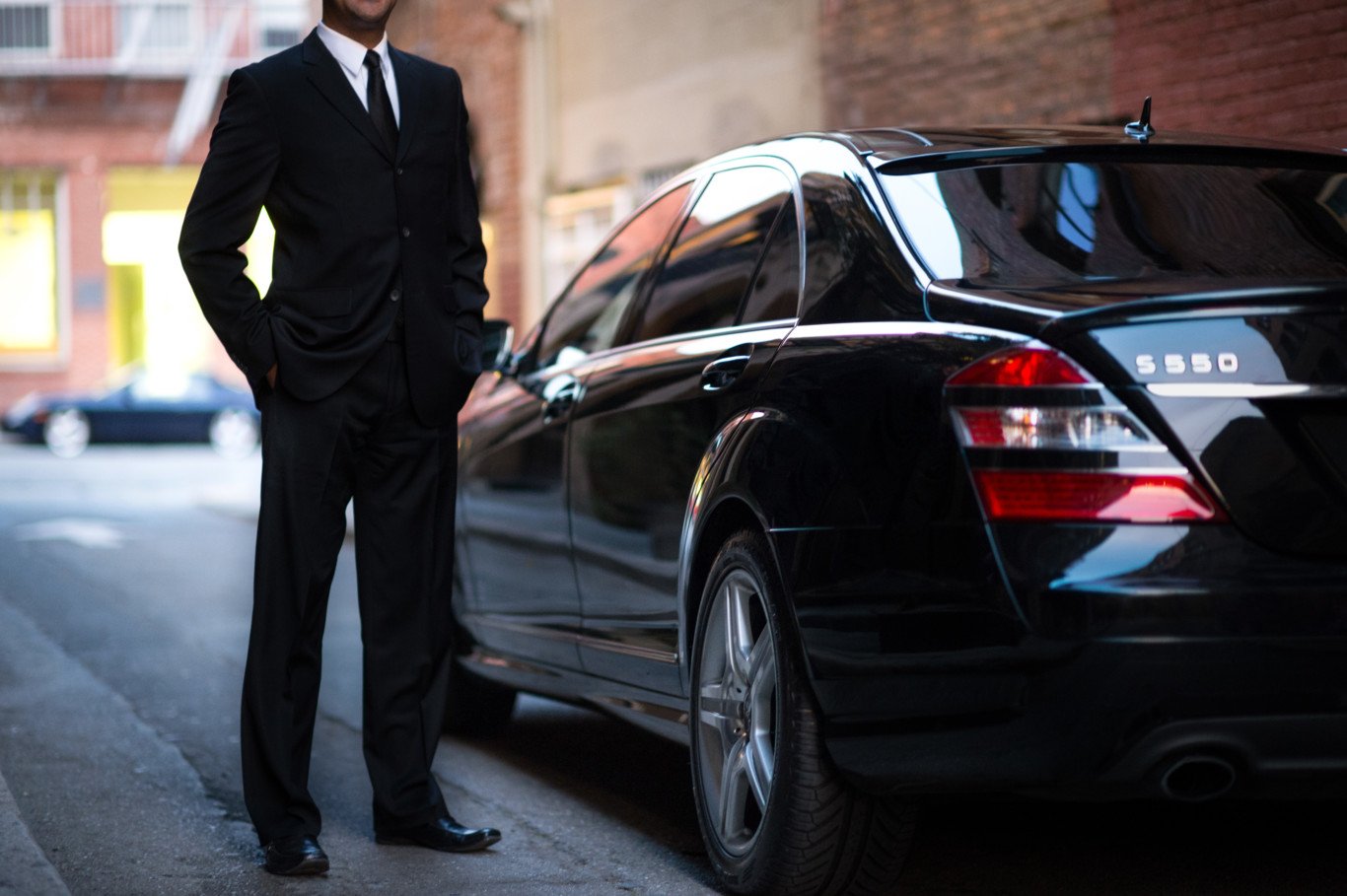 Professional chauffeur standing next to a luxury black Mercedes S-Class vehicle